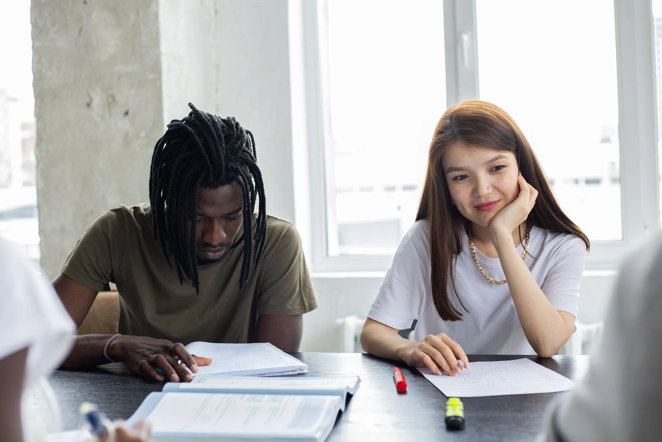 Students with notebooks and worksheets seated together at a classroom table.